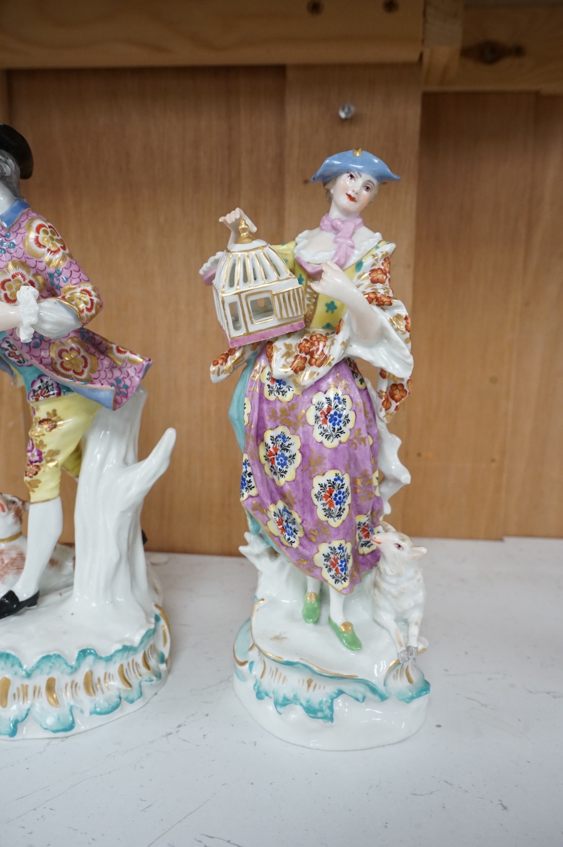 A pair of Derby style figures of a lady holding a bird cage and a gentleman holding a bird, tallest 23cm high